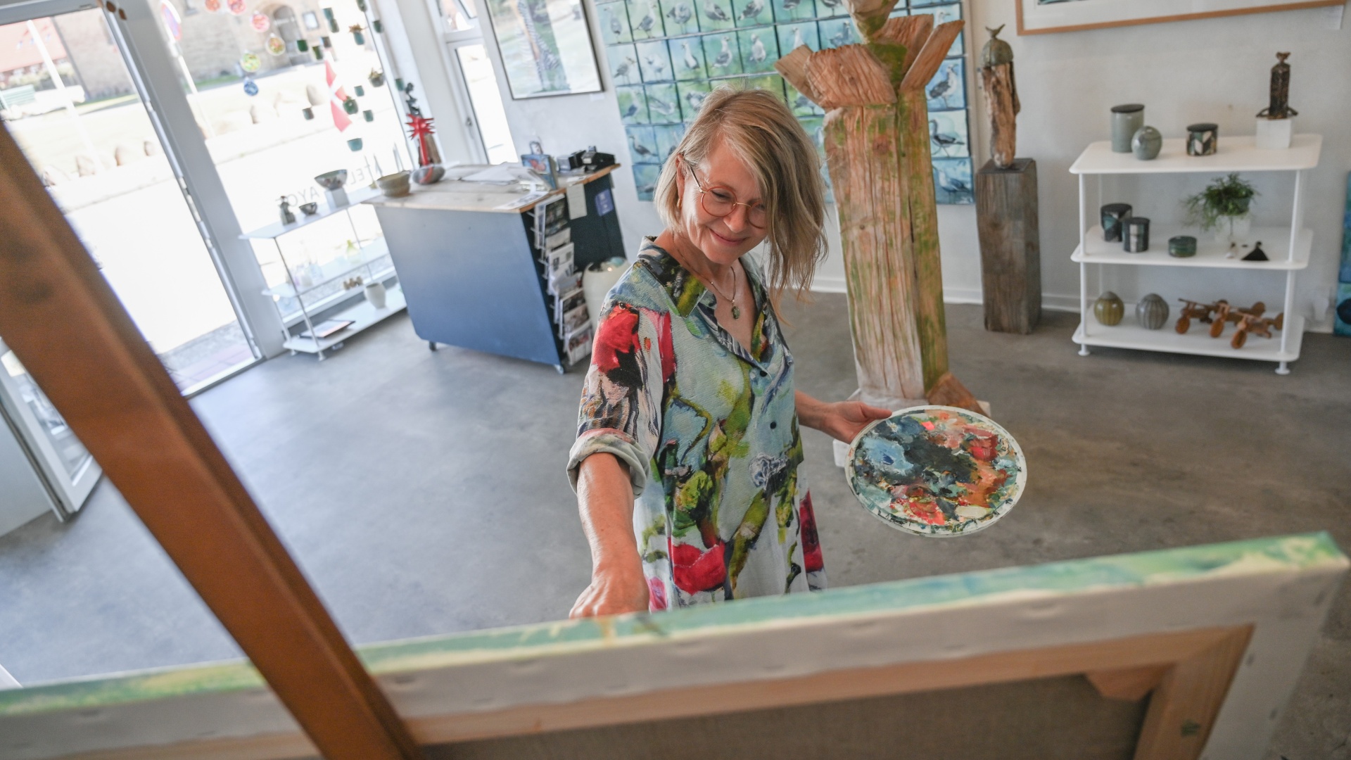 Kunstner maler ved staffeli i lyst galleri.