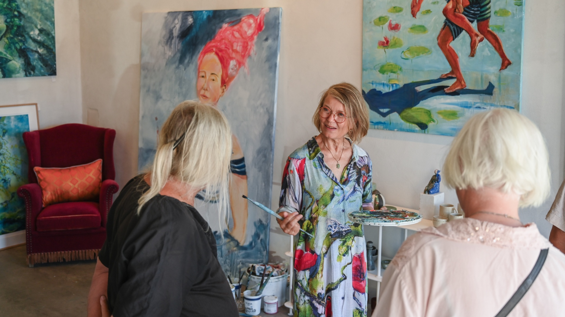 Kunstner viser sine malerier frem for besøgende i et galleri.