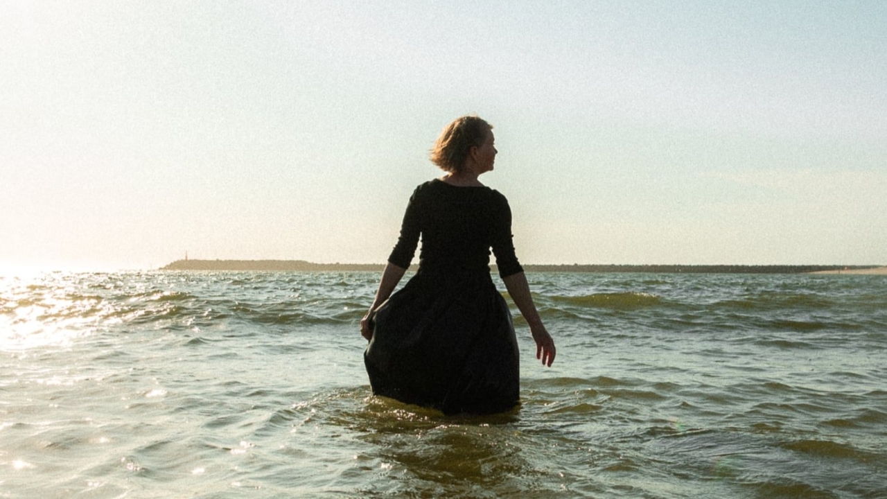 Kvinde står i havet med udsigt mod kysten.
