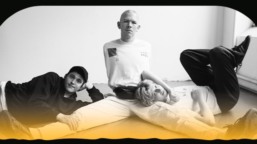 Det sort-hvide foto af tre musikere, der sidder sammen på gulvet i et rum.