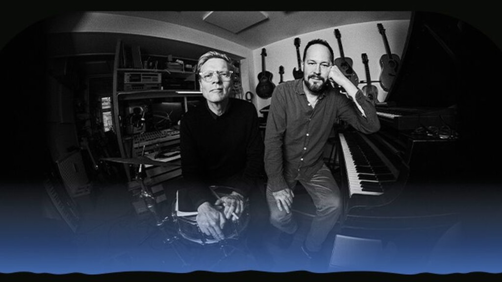 Det sort-hvide foto af to musikere, der står sammen foran flere musikinstrumenter.