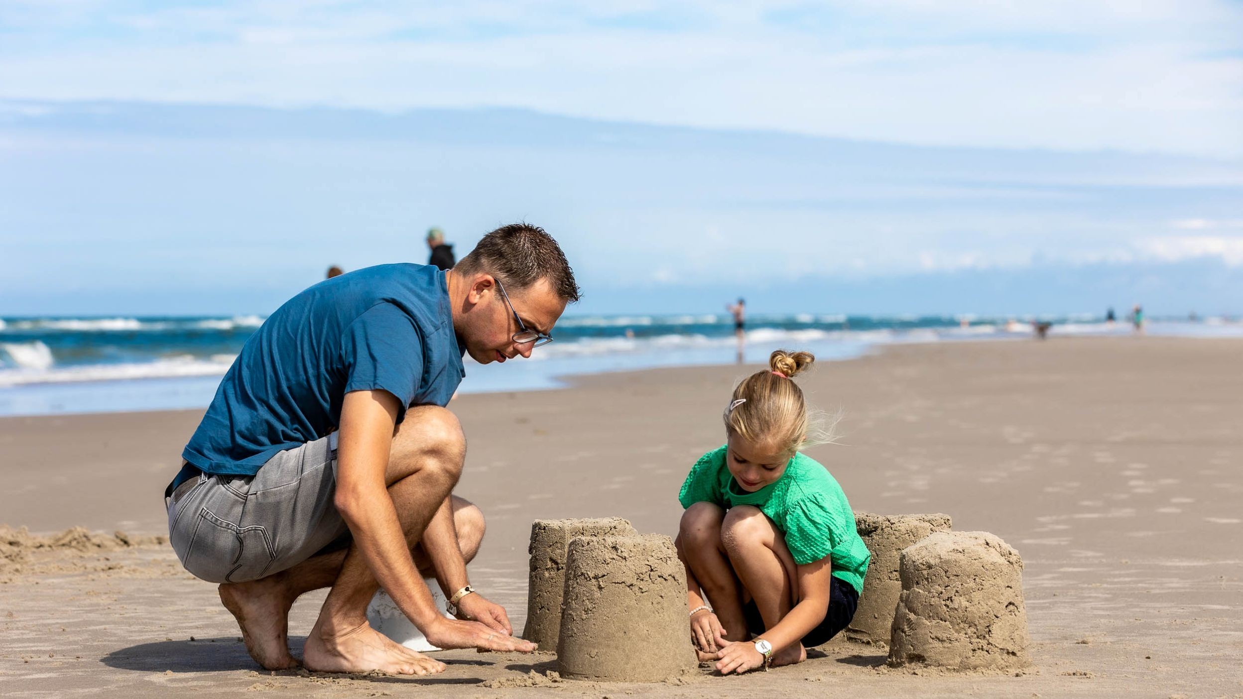 Father and daughter build a sandcastle on Vejers Strand by the North Sea waves.