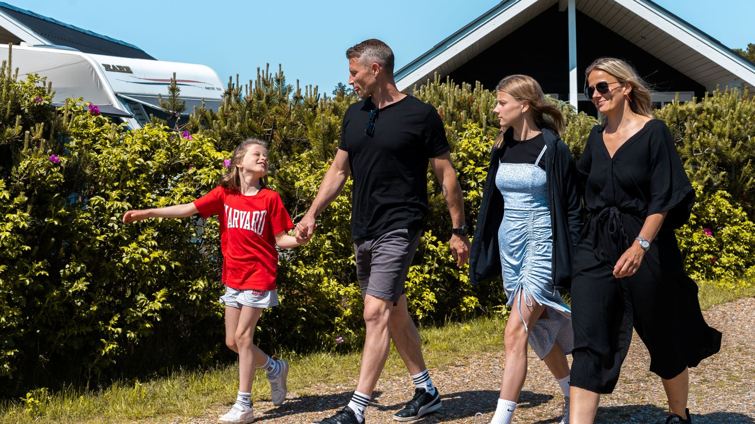 Family with two children on the campsite road between a caravan and holiday cabin in front of a natural hedge.