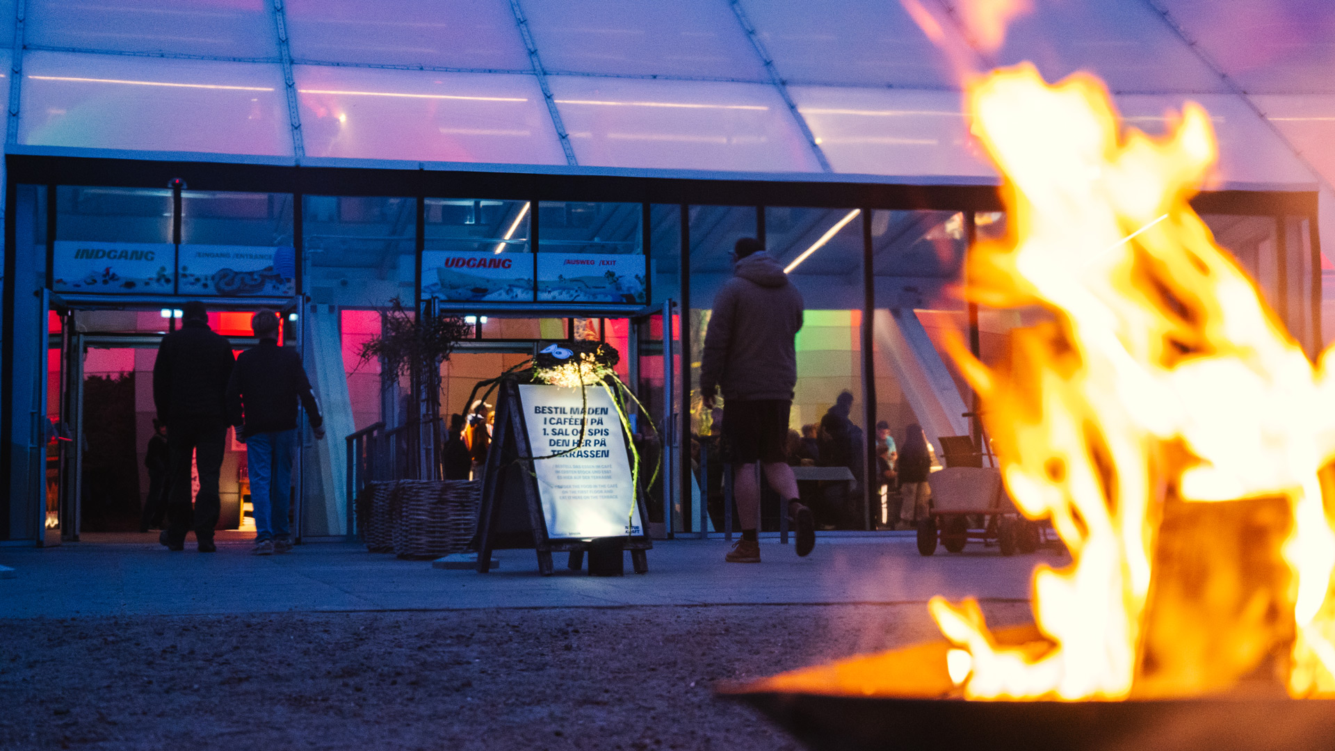 The entrance to Naturkraft in the evening with a fire in the foreground.
