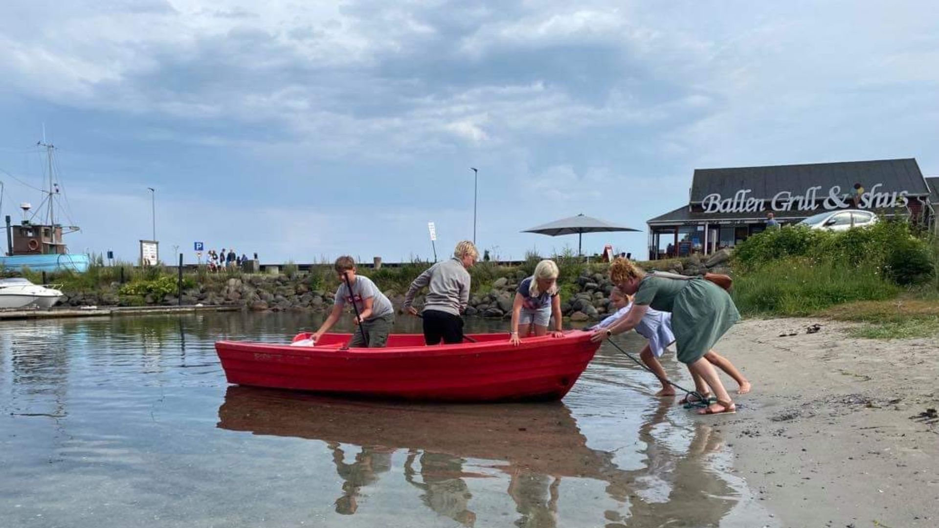 Familien Dolleris & Mikkelsen skubber en rød jolle i vandet på Ballen havn.