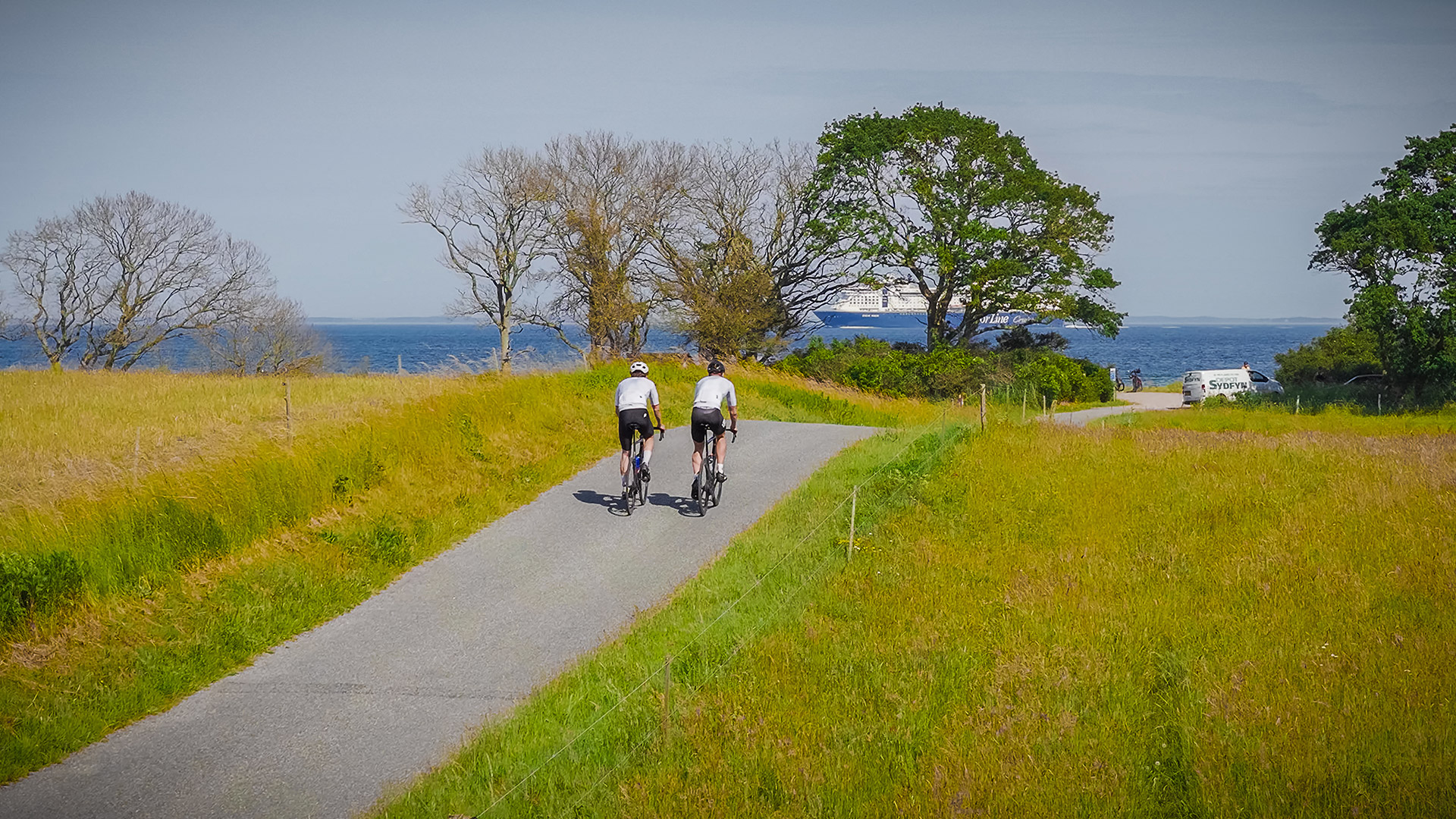 Two cyclists heading towards the coast with a large ship on the Great Belt in the background