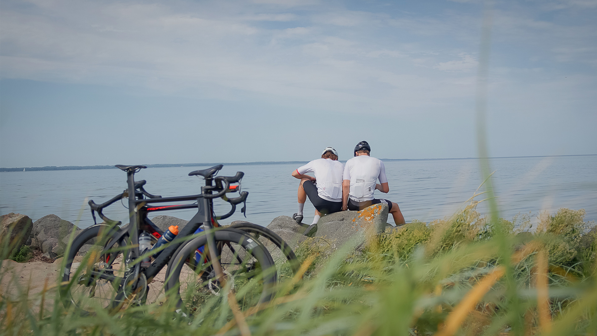 Zwei Radfahrer machen Pause auf den Steinen an der Küste, ihre Fahrräder stehen im Vordergrund