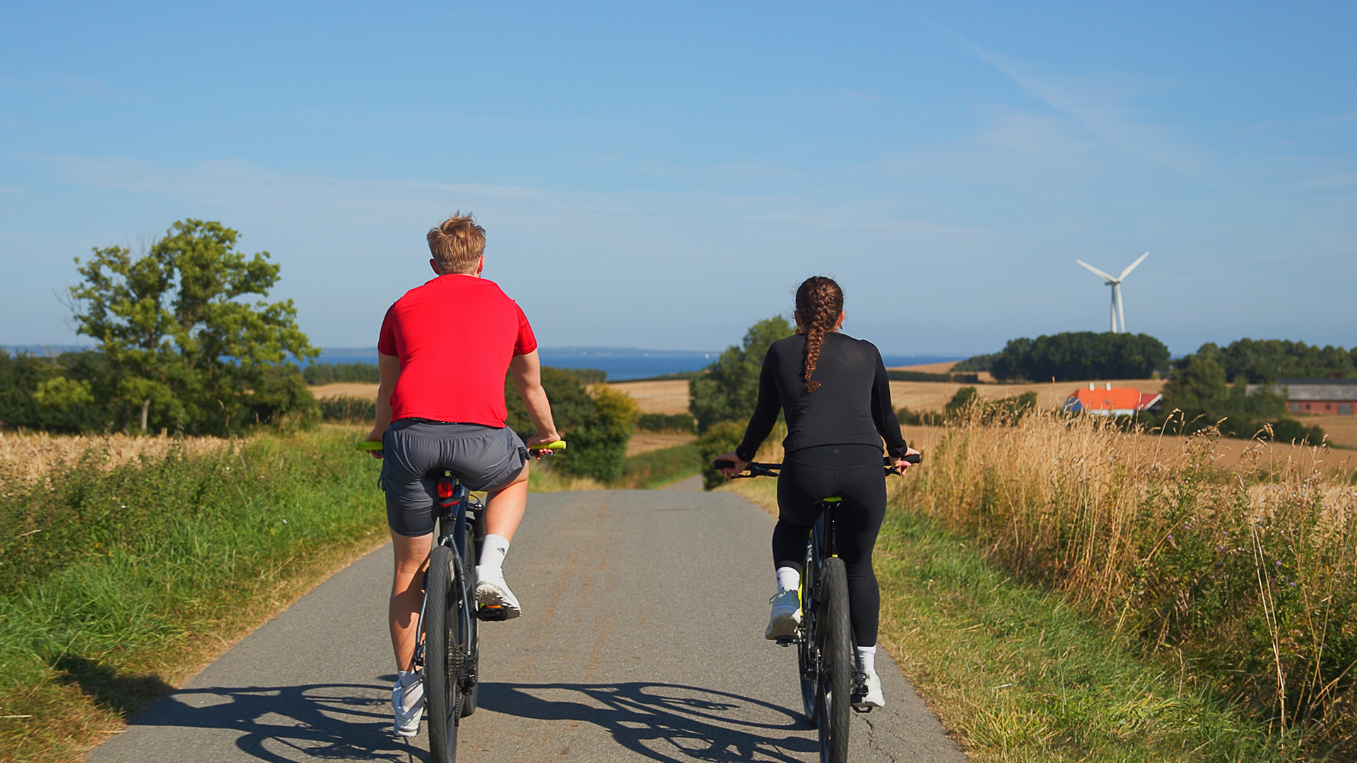 Two cyclists on a country road through the open landscape of northern Langeland with the sea in the background