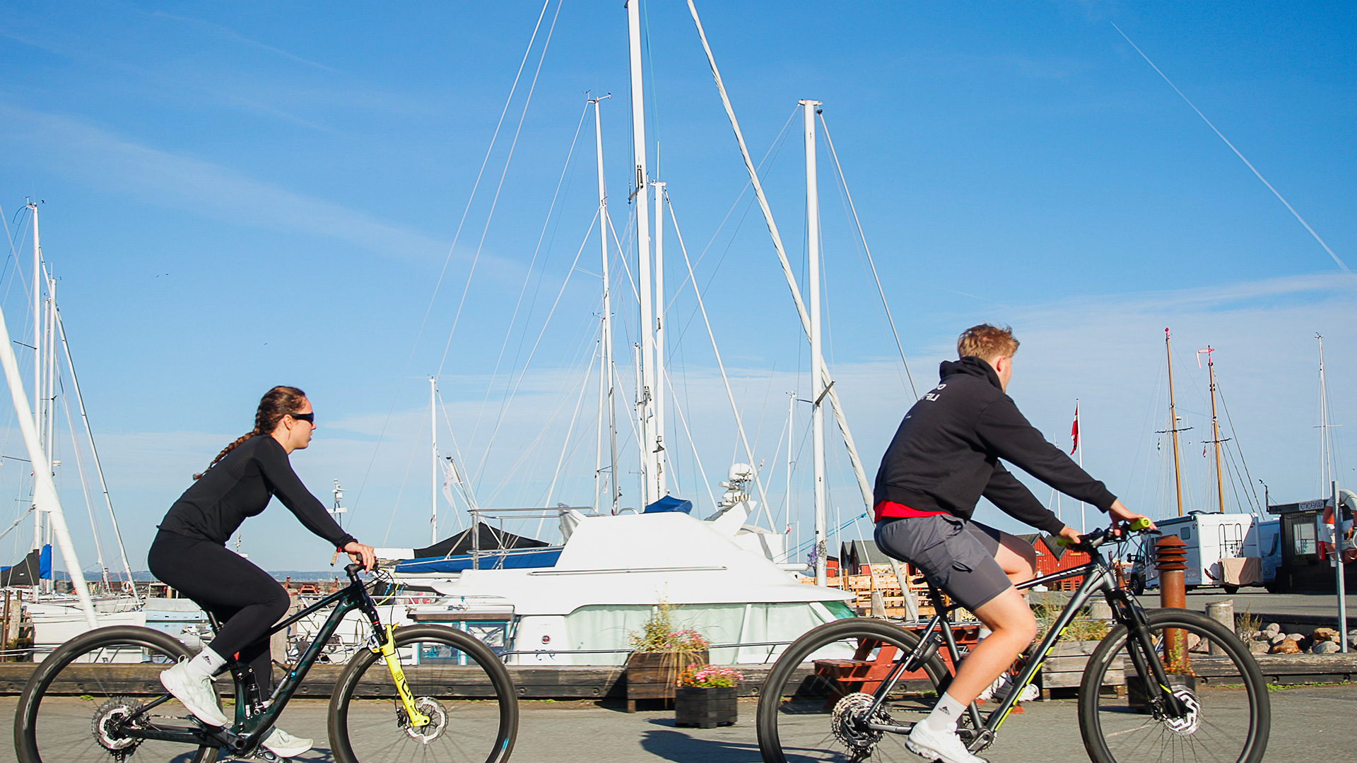 To cyklister på Lohals Havn med sejlbåde i baggrunden