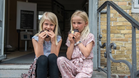 To piger sidder på trappesten og nyder at spise honningkage