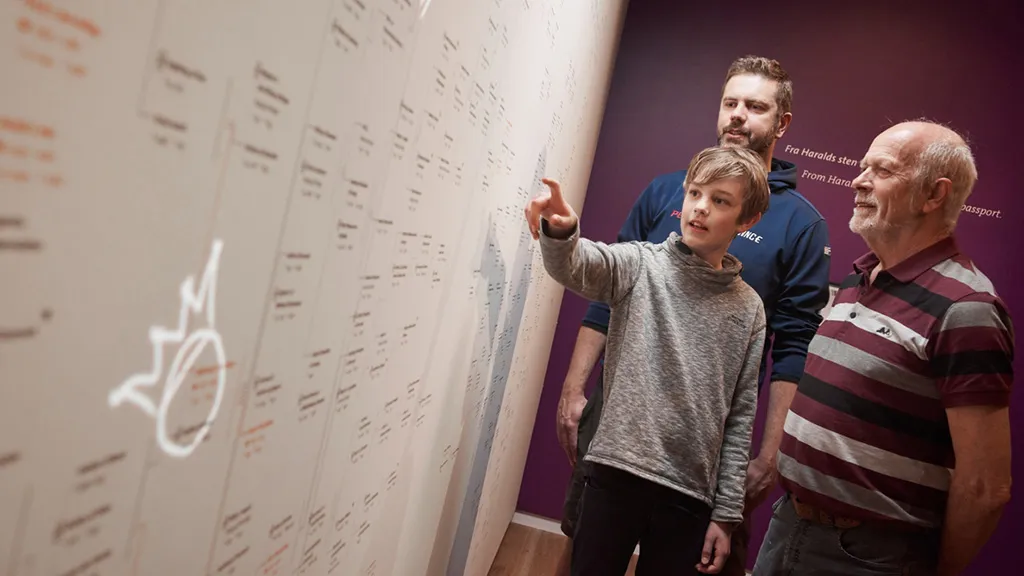 Father, grandfather and son looking at an overview of the Danish monarchs.