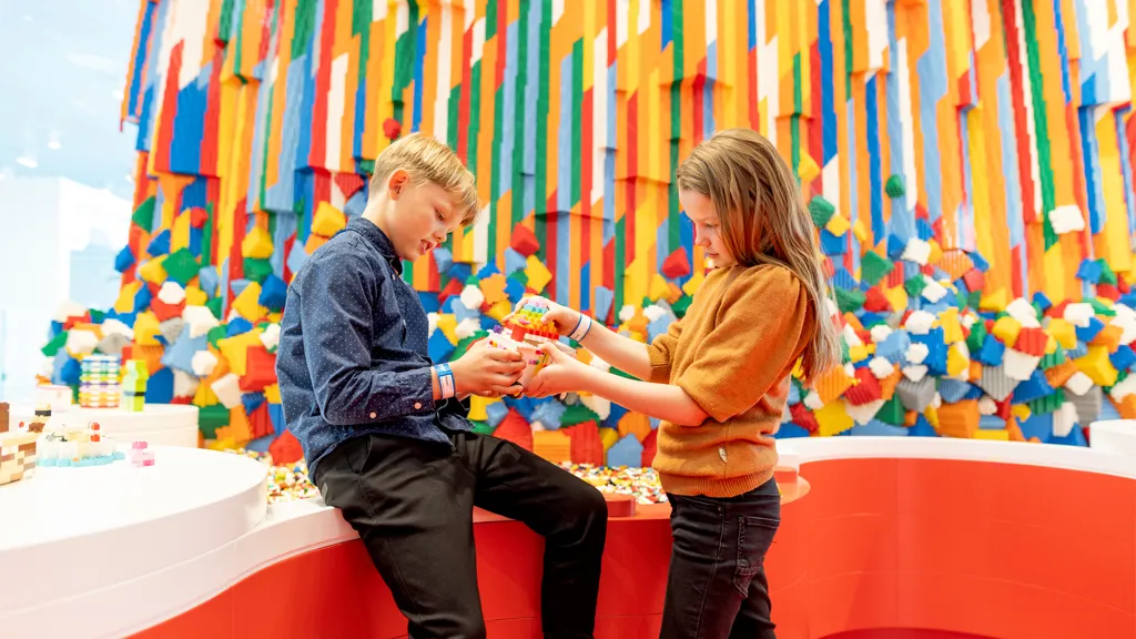Two children building with LEGO® bricks in front of the LEGO Waterfall in LEGO House