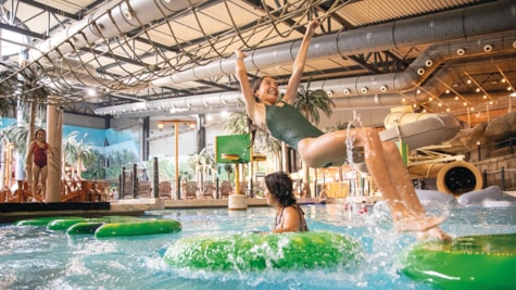 En pige svinger sig i et net over vandet i Aquadome activity pool i Lalandia Billund, mens andre børn leger i baggrunden.