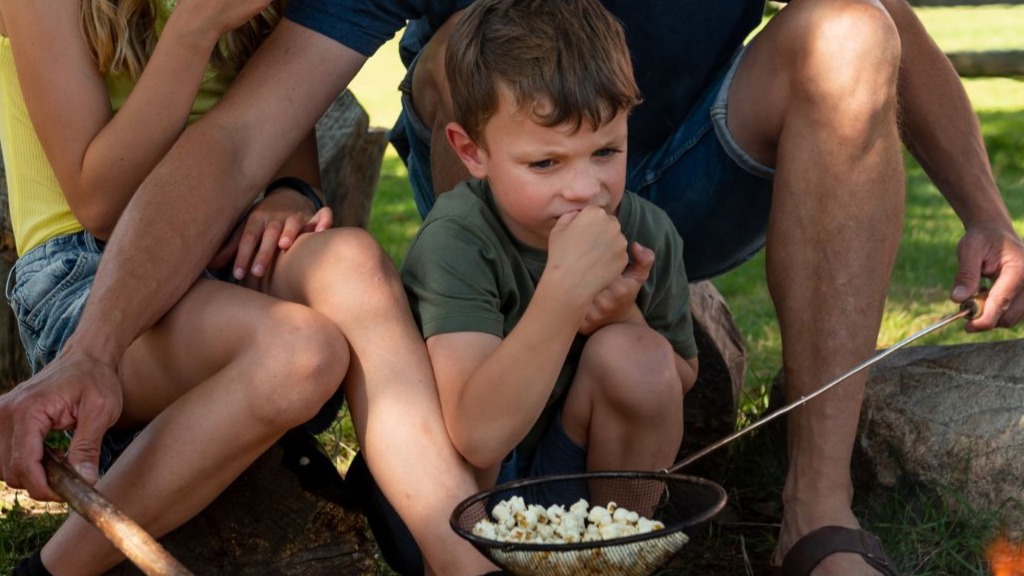 A little boy watching dad popping popcorn over a bonfire