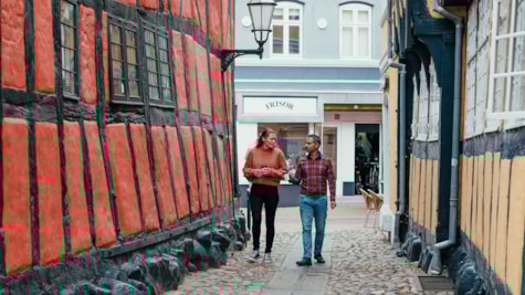 To personer går gennem en smal brostensgyde omgivet af farverige bindingsværkshuse i Kolding.
