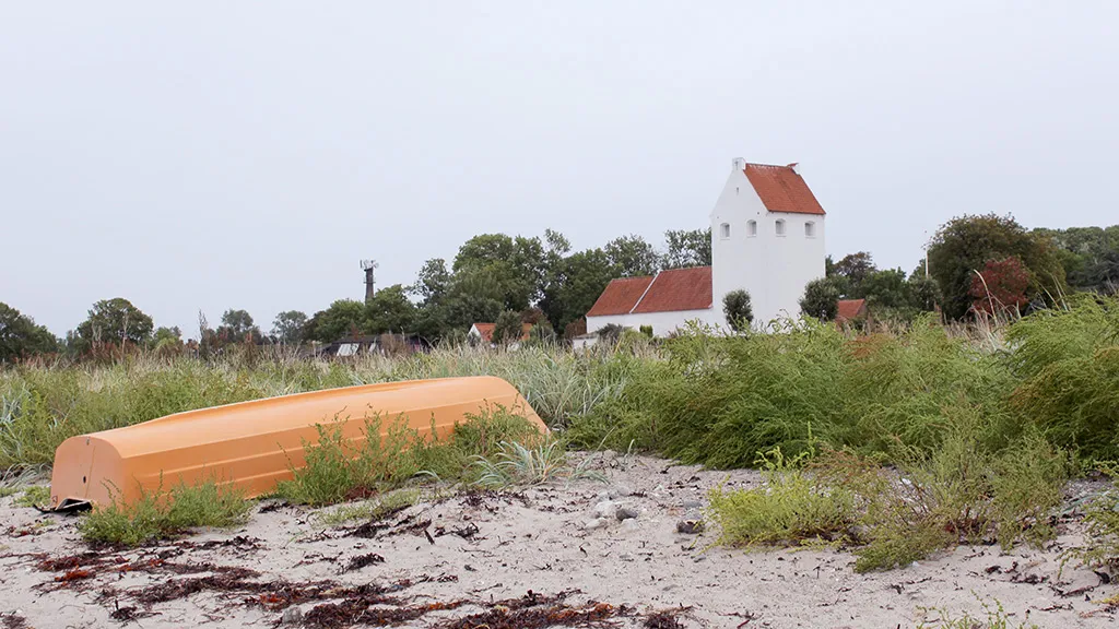 A rowing boat on the beach with Endelave Church in the background