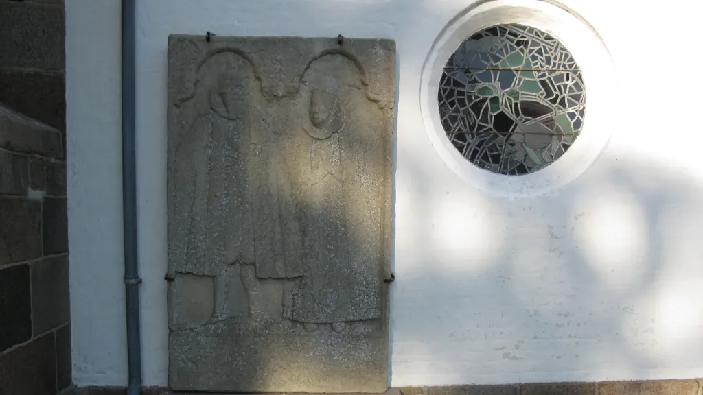 Mindesten i muren på Gosmer Kirke og mosaikvindue