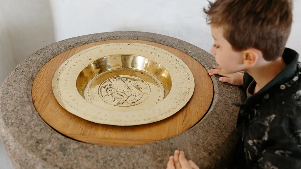 Dreng står foran døbefonden i Hjarnø Kirke