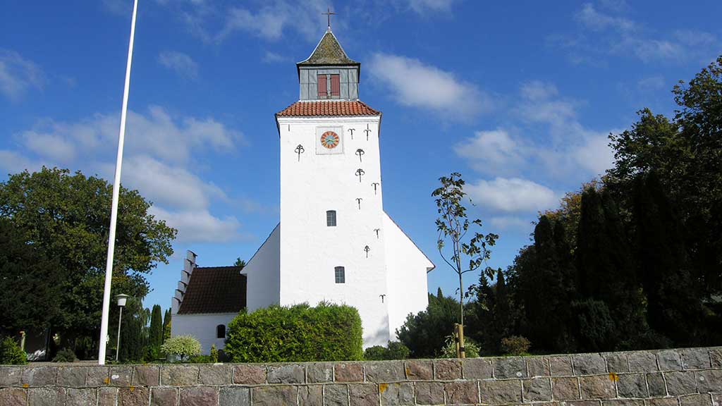 Church tower viewed from a stone fence with a blue sky and flagpole