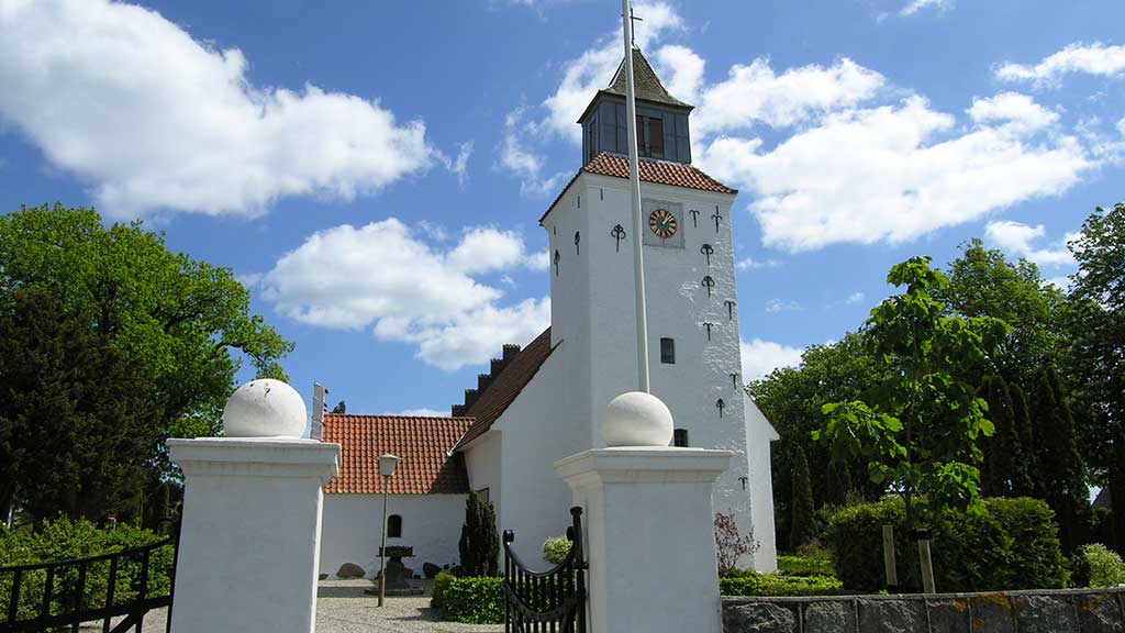 The entrance of Saksild Church and the church's front facade, surrounded by green trees