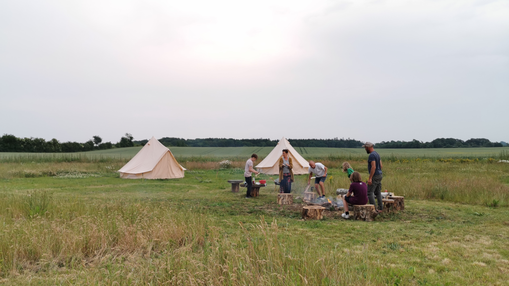 Two glamping tents in a field with a campfire area