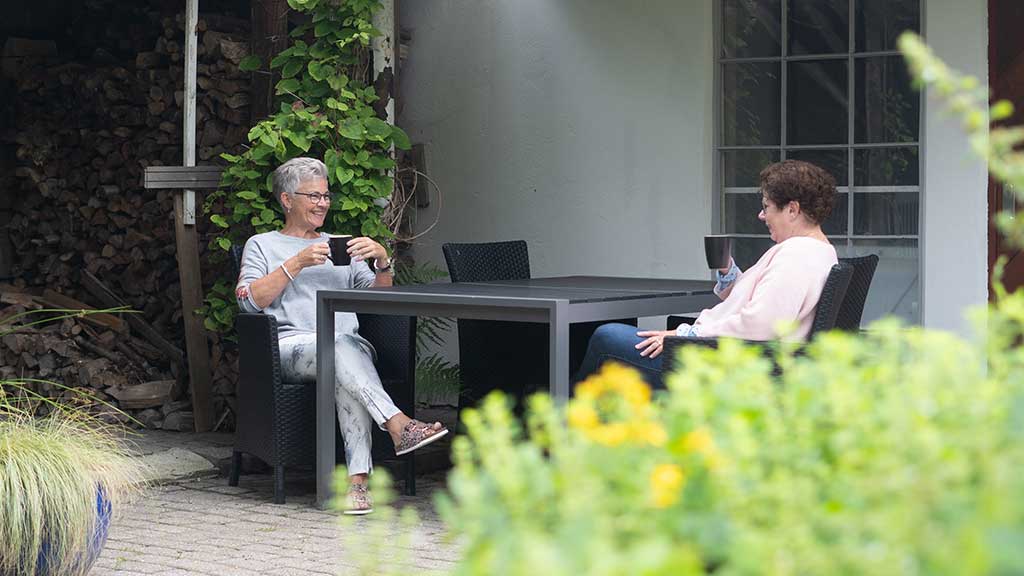 Two women drink coffee and chat together at a garden table