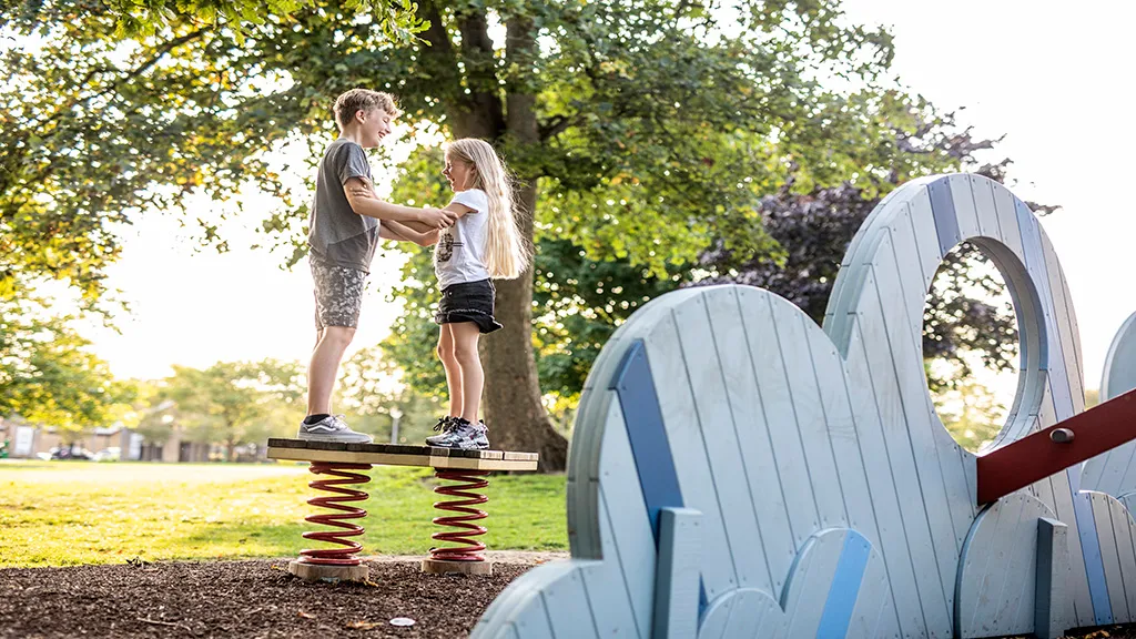 Two children standing and holding each other on a seesaw at a playground