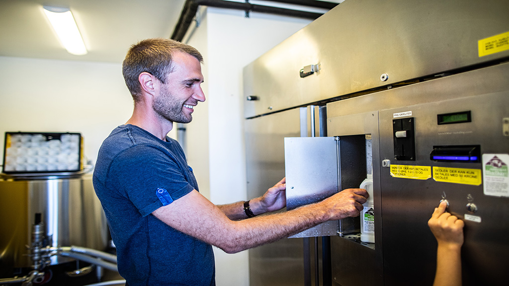 A man is dispensing milk from a machine at Vejlskovgaard Dairy