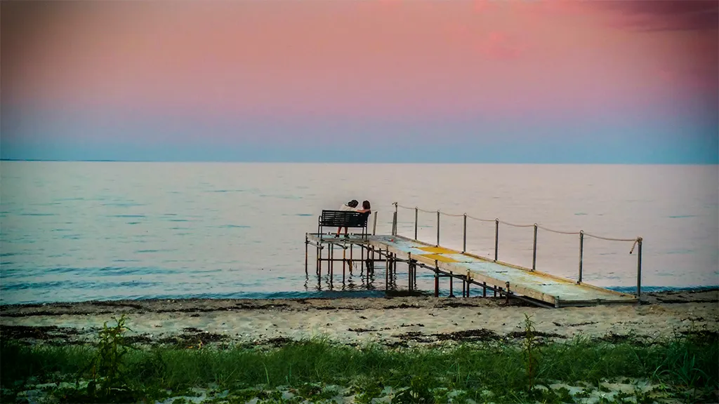 Par nyder solnedgangens farver på badebroen ved Storstranden