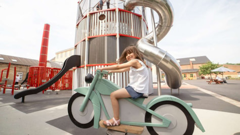 Pige sidder på motorcykel vippe på industri museets legeplads