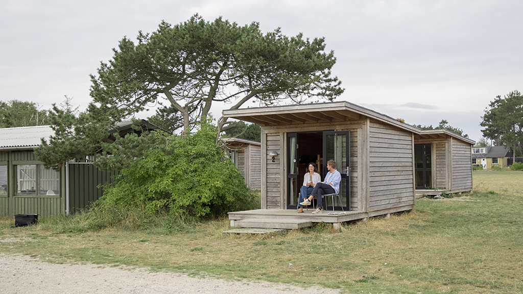 A man and a woman in their 30s are sitting in front of a cabin at the Tunø Campsite and chatting