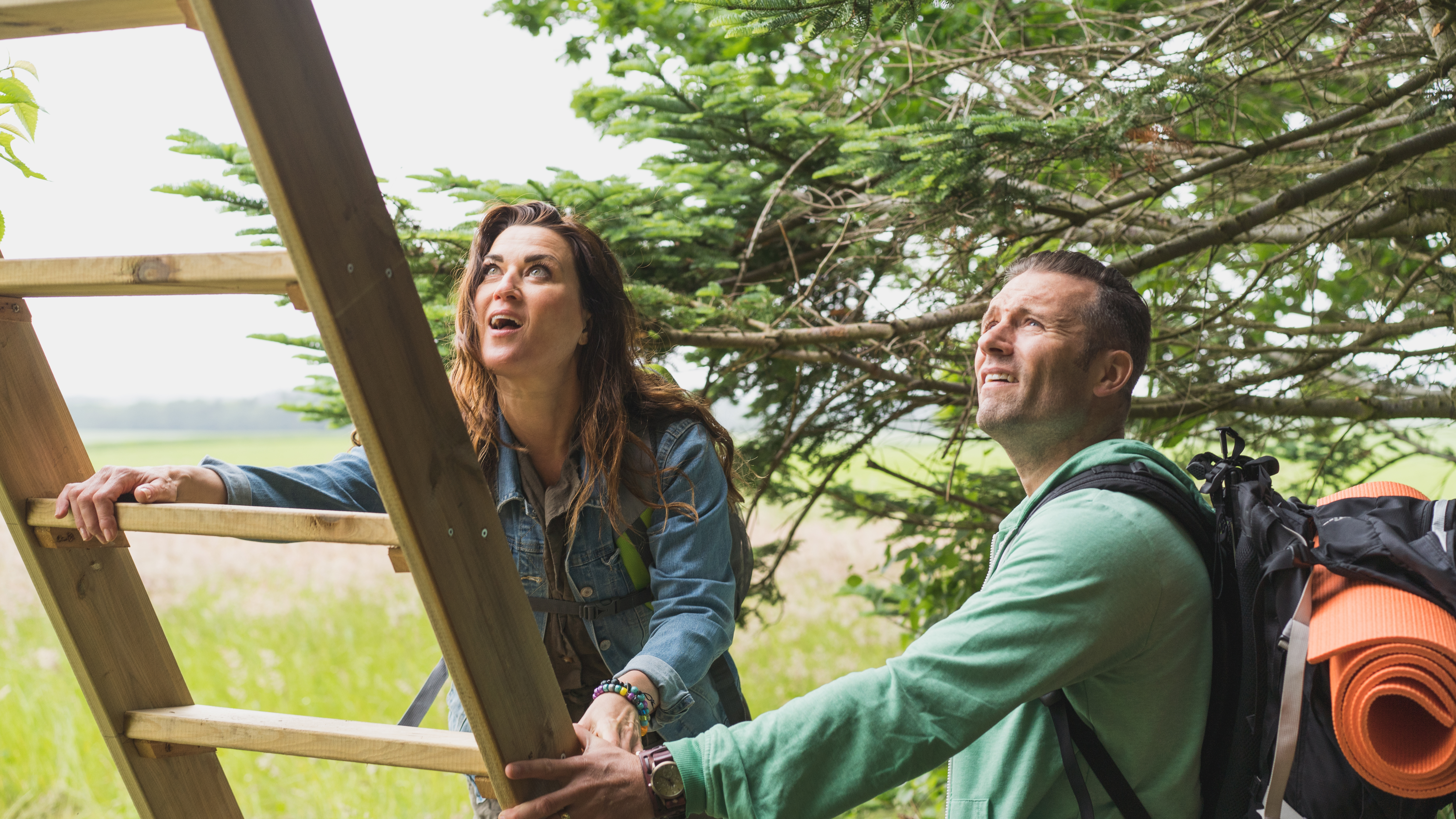A couple climbing a ladder to a tree-top shelter at Holmely