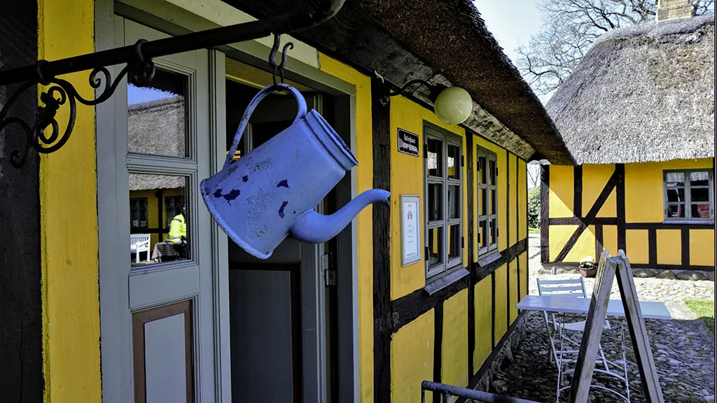 Blå kaffekande hænger i krog ved gult hus med bindingsværk og stråtag på Hjortsvang Museum tæt på Uldum og Gudenåen