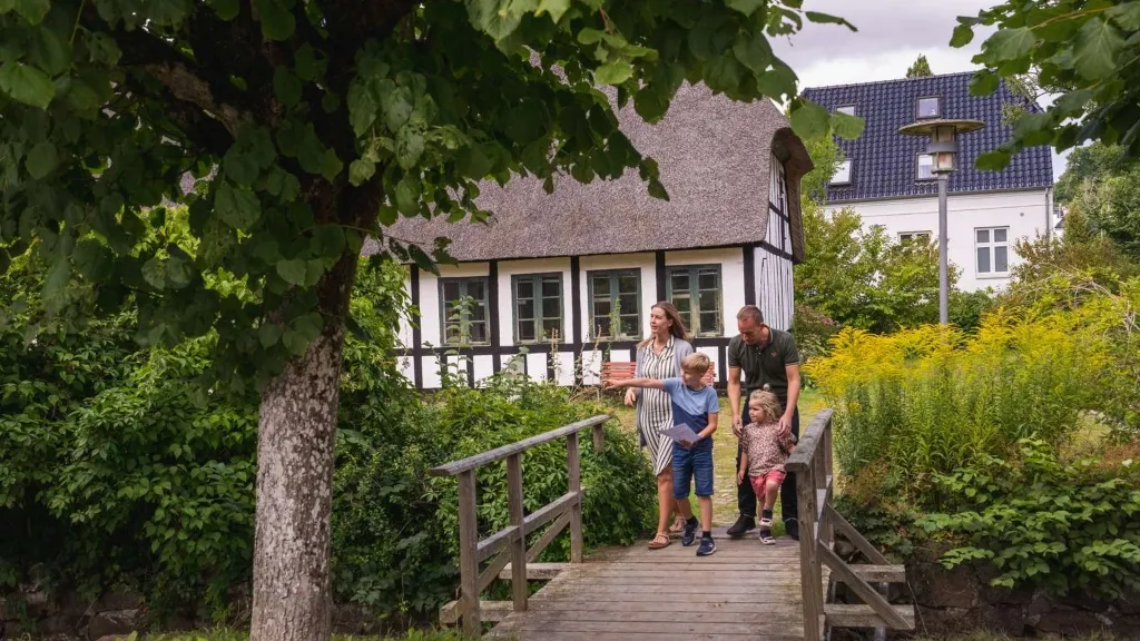 Familie går over bro ved gammelt hvidkalket bindingsværkshus