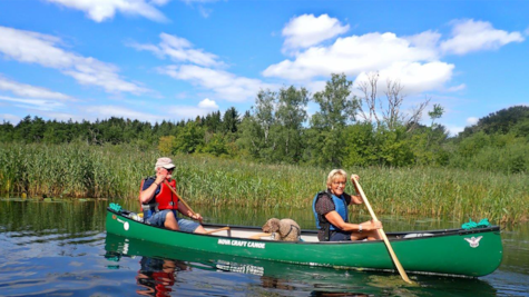 Par sejler i kano på Gudenåen med deres hund som passager
