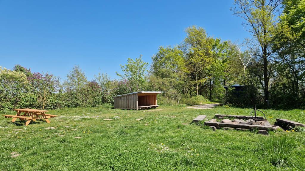 The campsite in Brigsted with shelter, table and bench set, campfire site, and toilet