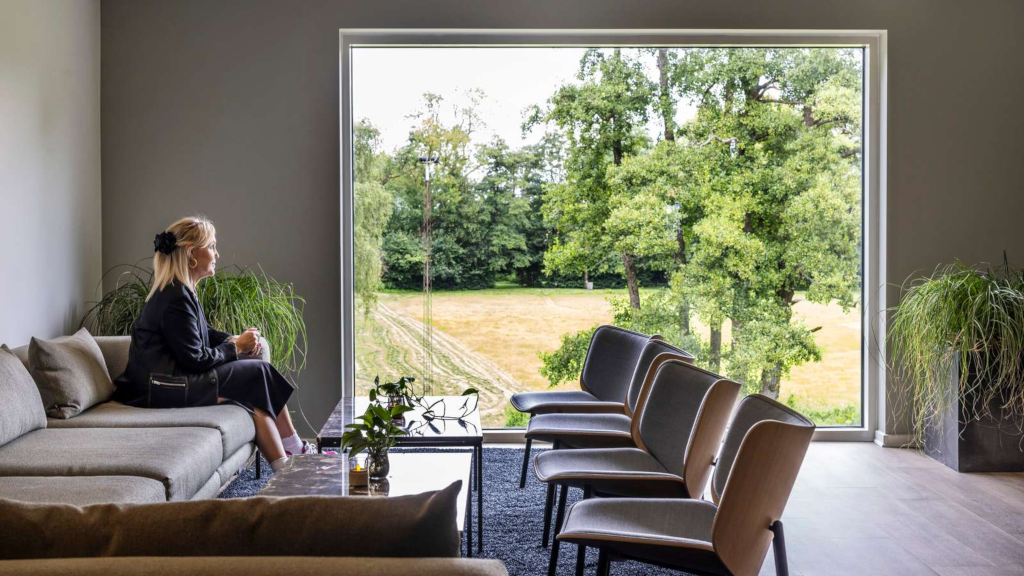 A woman sitting on a sofa at Comwell Bygholm Park, looking at the park through the window