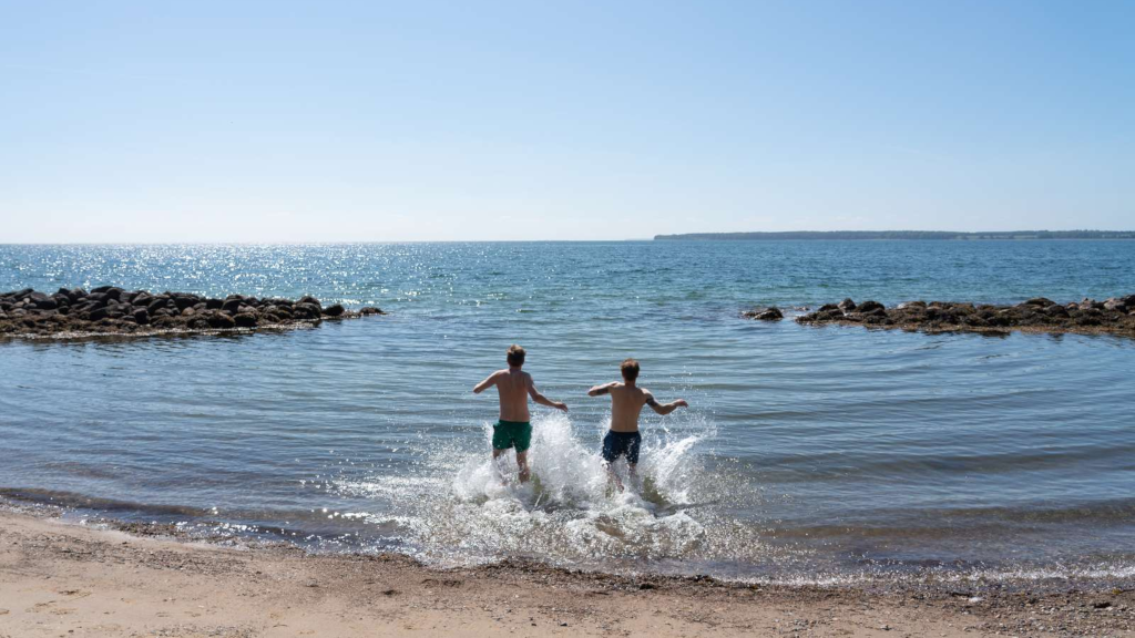 Two boys running into the water at As Vig Beach on a summer day
