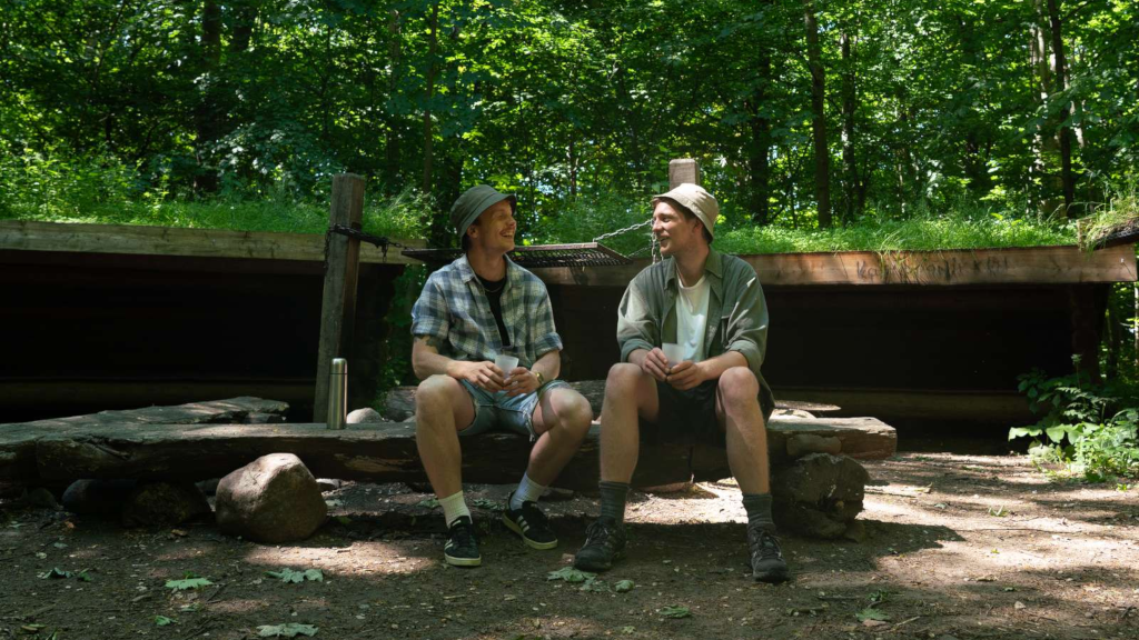 Two men sitting on a bench in front of the shelters at Tønballe Shelter Site