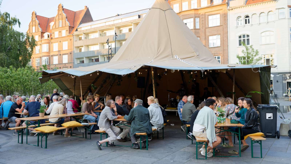 People sitting on benches by a tent at Torvet in Horsens during the Horsens Holder festival