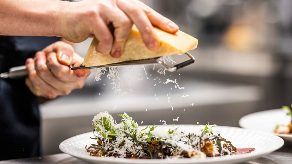 Chef grating parmesan over a plated salad