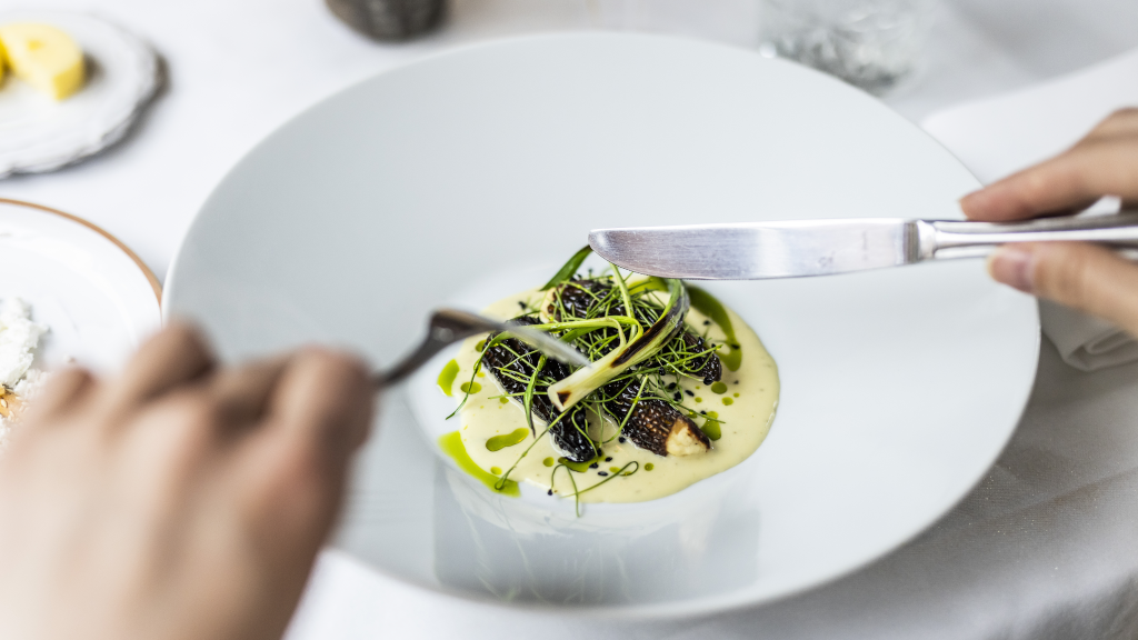 A person eats a gourmet dish in a deep plate with a knife and fork at Ji-Mi's in Horsens