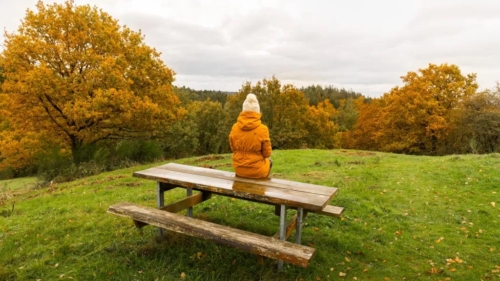 Kvinde sidder på et bord/bænkesæt i Trustrup Udsigtshøje i regnvejr