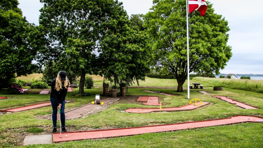 Kvinde spiller minigolf ved et Dannebrog og med havudsigt hos Stalden Tunø Minigolf