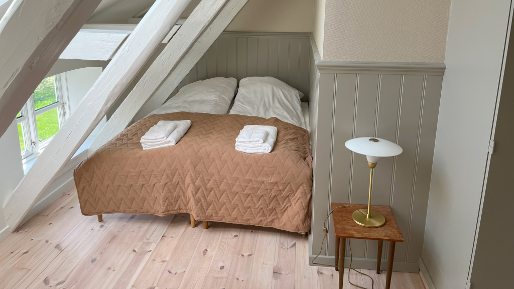 A double bed in a corner under a sloped wall at Reballegaard
