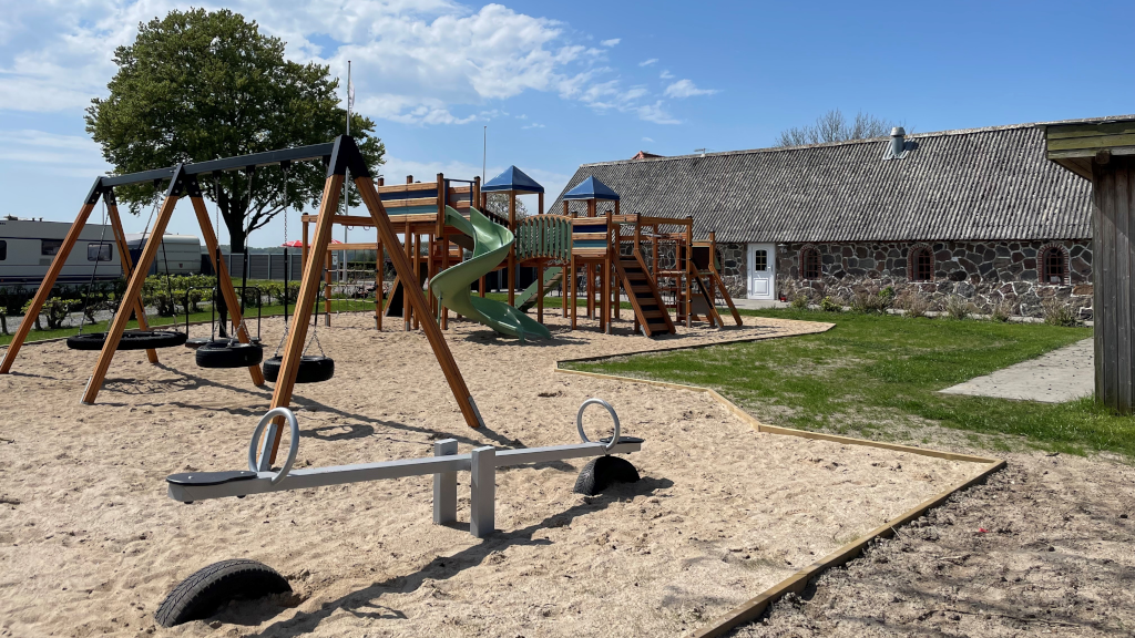 Swing set, climbing tower, and seesaw at the playground at Hjarnø Camping