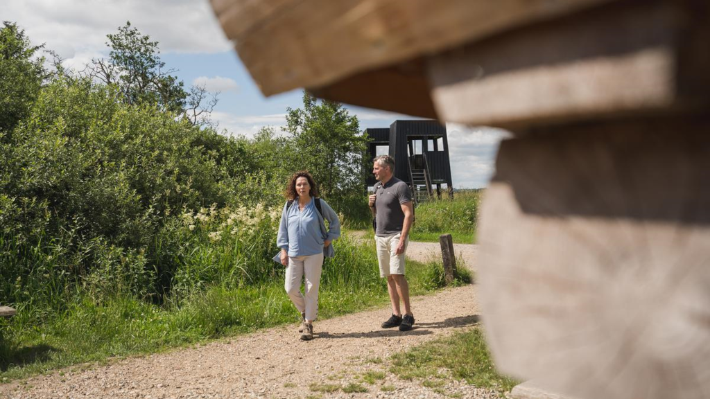 A couple hiking towards a shelter at Uldum Marsh with the birdwatching tower in the background.