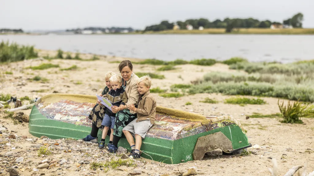 A mother sitting on a boat on the beach at Hjarnø with three boys, looking at the treasure map for the Hjarnø Round Treasure Hunt