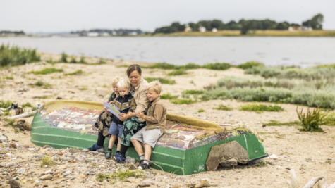 Mor sidder på båd på strand på Hjarnø med tre drenge og kigger på skattekortet for Skattejagten Hjarnø Rundt