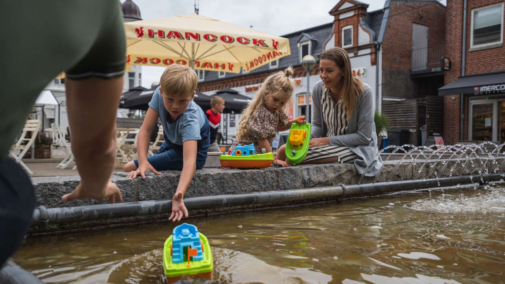 Family sitting by a fountain at the town square in Odder while children play with toys